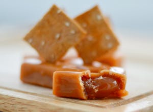 A detailed view of caramel toffee with crackers on a wooden board.
